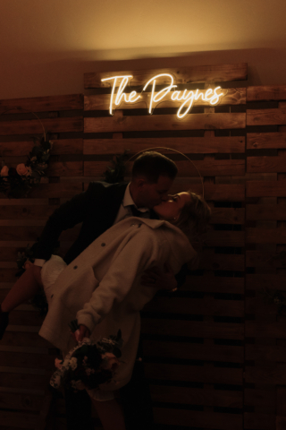 A couple in their wedding attire on their wedding day take their romantic and natural documentary styled photos in front of their personalized neon sign. Photographed by Hannah Lylene Photography.