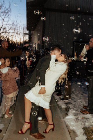 A couple in their wedding attire on their wedding day have a flash photography exit using a bubble machine. Photography by Hannah Lylene Photography.