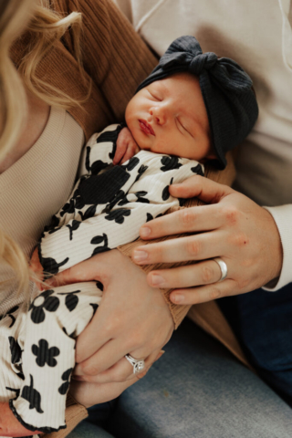 A young couple holds their newborn baby in an indoor studio wearing  neutral color matching outfits. Photography by Hannah Lylene Photography.