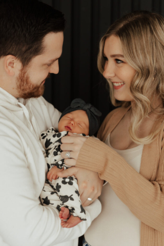 A young couple holds their newborn baby in an indoor studio wearing  neutral color matching outfits. Photography by Dallas Photographer Hannah Lylene Photography