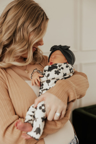 A young mother holds their newborn baby in an indoor studio wearing neutral color matching outfits. Photography by Dallas Photographer Hannah Lylene Photography