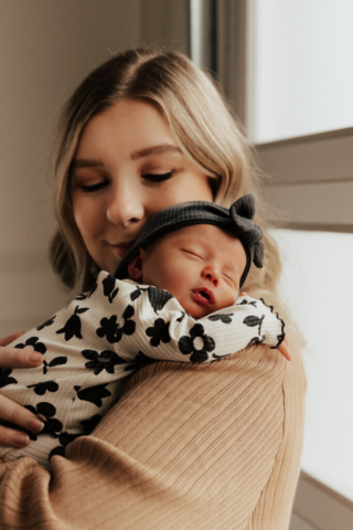 A young mother holds their newborn baby in an indoor studio wearing neutral color matching outfits. Photography by Dallas Photographer Hannah Lylene Photography
