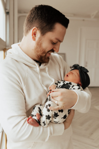 A young father holds their newborn baby in an indoor studio wearing neutral color matching outfits. Photography by Dallas Photographer Hannah Lylene Photography