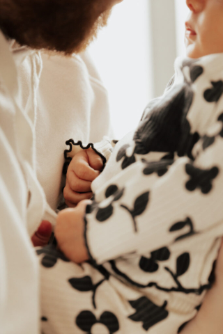A young father holds their newborn baby in an indoor studio wearing neutral color matching outfits. Photography by Dallas Photographer Hannah Lylene Photography