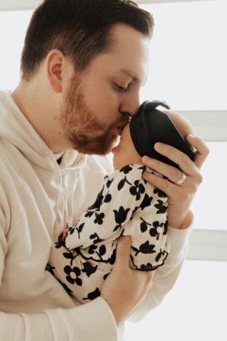 A young father holds their newborn baby in an indoor studio wearing neutral color matching outfits. Photography by Dallas Photographer Hannah Lylene Photography
