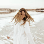 A woman in all white attire spins around a frozen lake for a self portrait. Photography by Hannah Lylene Photography.