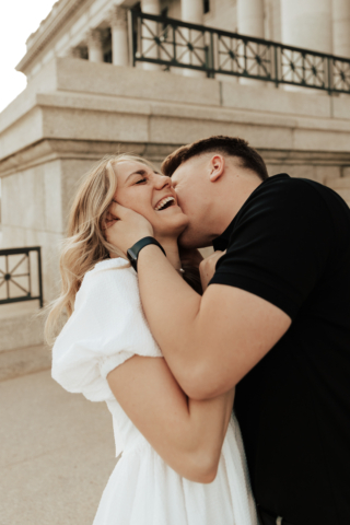 A couple in neutral attire in downtown Dallas Texas kiss and run around for engagement photos. Photography by Hannah Lylene Photography.