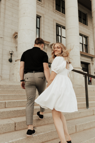 A couple in neutral attire in downtown Dallas Texas kiss and run around for engagement photos. Photography by Hannah Lylene Photography.