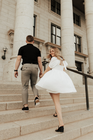 A couple in neutral attire in downtown Dallas Texas kiss and run around for engagement photos. Photography by Hannah Lylene Photography.