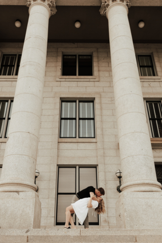 A couple in neutral attire in downtown Dallas Texas kiss and run around for engagement photos. Photography by Hannah Lylene Photography.