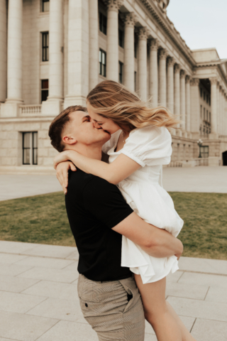 A couple in neutral attire in downtown Dallas Texas kiss and run around for engagement photos. Photography by Hannah Lylene Photography.