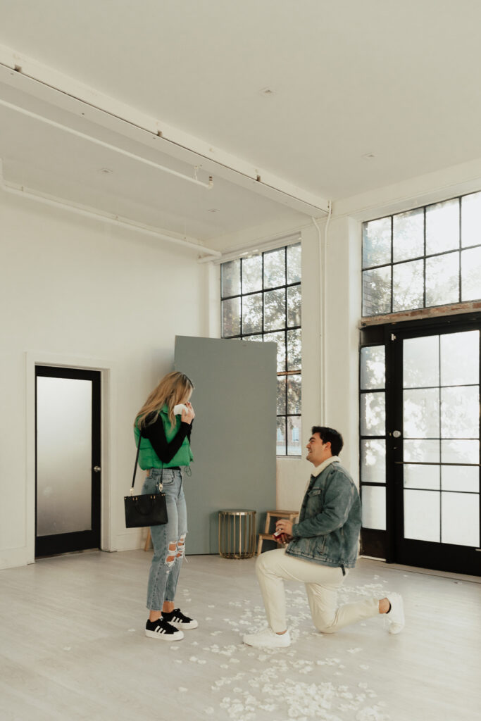 A couple in neutral attire at the Lumen Room Studio in Fort Worth, Texas get engaged surrounded by baby&rsquo;s breath. Photography by Hannah Lylene Photography.