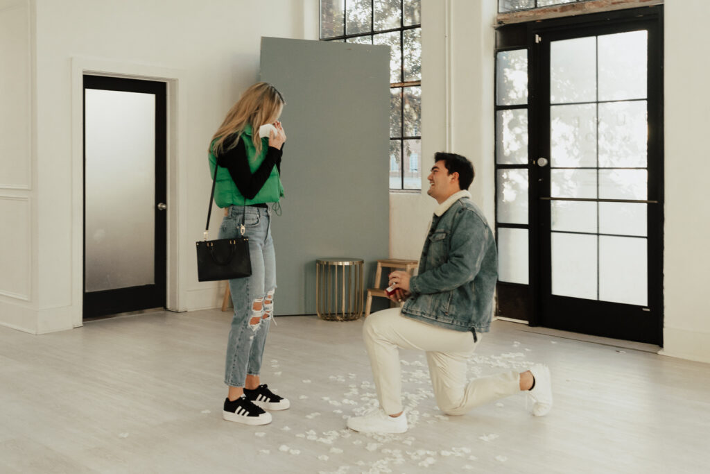 A couple in neutral attire at the Lumen Room Studio in Fort Worth, Texas get engaged surrounded by baby&rsquo;s breath. Photography by Hannah Lylene Photography.