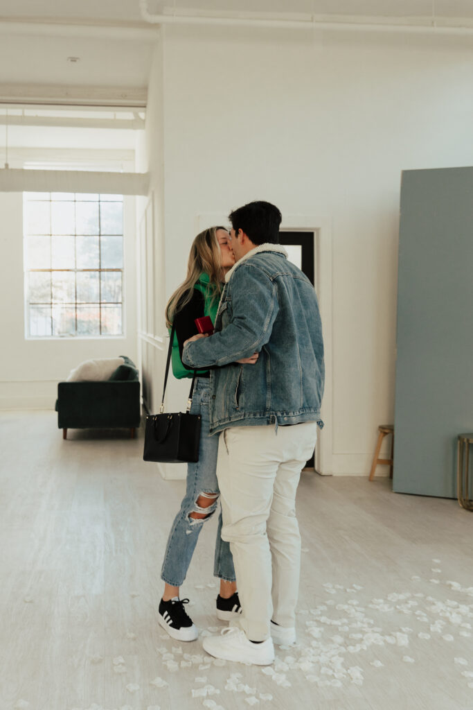 A couple in neutral attire at the Lumen Room Studio in Fort Worth, Texas get engaged surrounded by baby&rsquo;s breath. Photography by Hannah Lylene Photography.