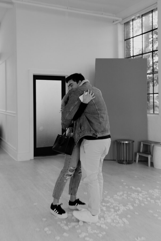 A couple in neutral attire at the Lumen Room Studio in Fort Worth, Texas get engaged surrounded by baby&rsquo;s breath. Photography by Hannah Lylene Photography.