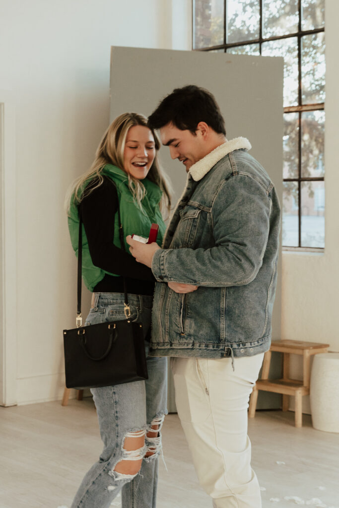 A couple in neutral attire at the Lumen Room Studio in Fort Worth, Texas get engaged surrounded by baby&rsquo;s breath. Photography by Hannah Lylene Photography.