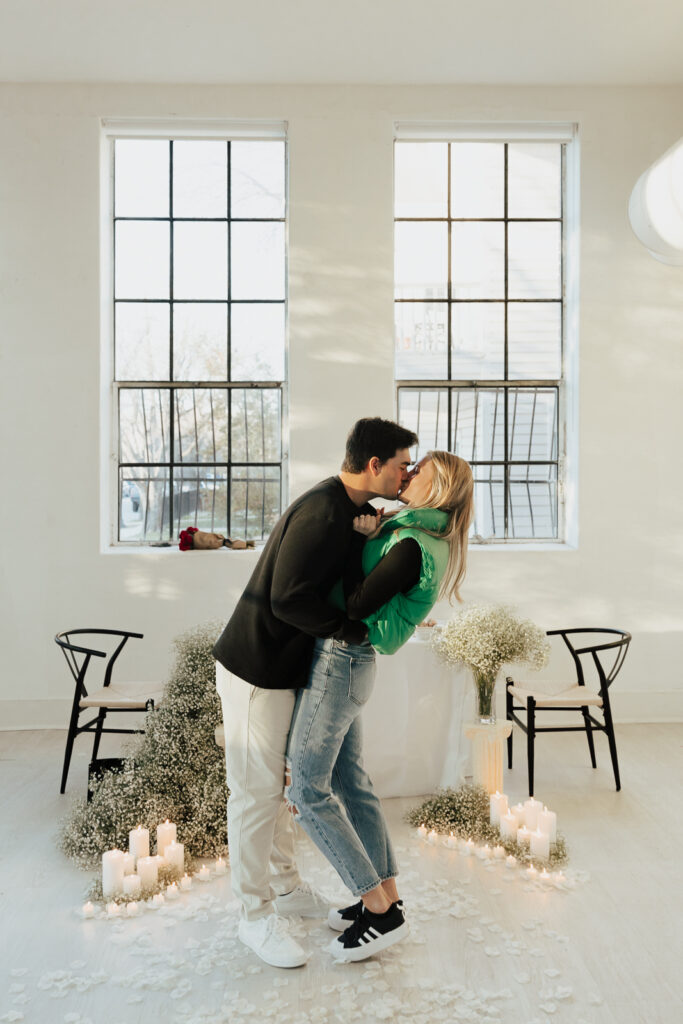 A couple in neutral attire at the Lumen Room Studio in Fort Worth, Texas get engaged surrounded by baby&rsquo;s breath. Photography by Hannah Lylene Photography.