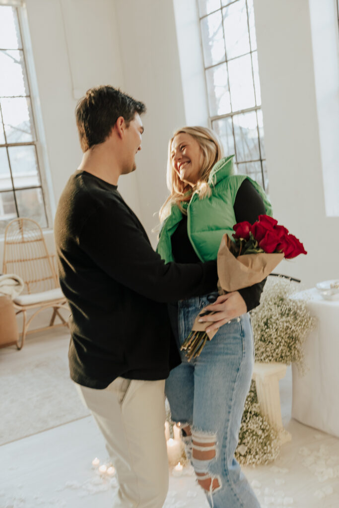 A couple in neutral attire at the Lumen Room Studio in Fort Worth, Texas get engaged surrounded by baby&rsquo;s breath. Photography by Hannah Lylene Photography.