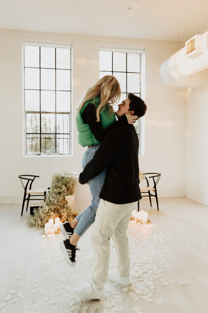 A couple in neutral attire at the Lumen Room Studio in Fort Worth, Texas get engaged surrounded by baby&rsquo;s breath. Photography by Hannah Lylene Photography.