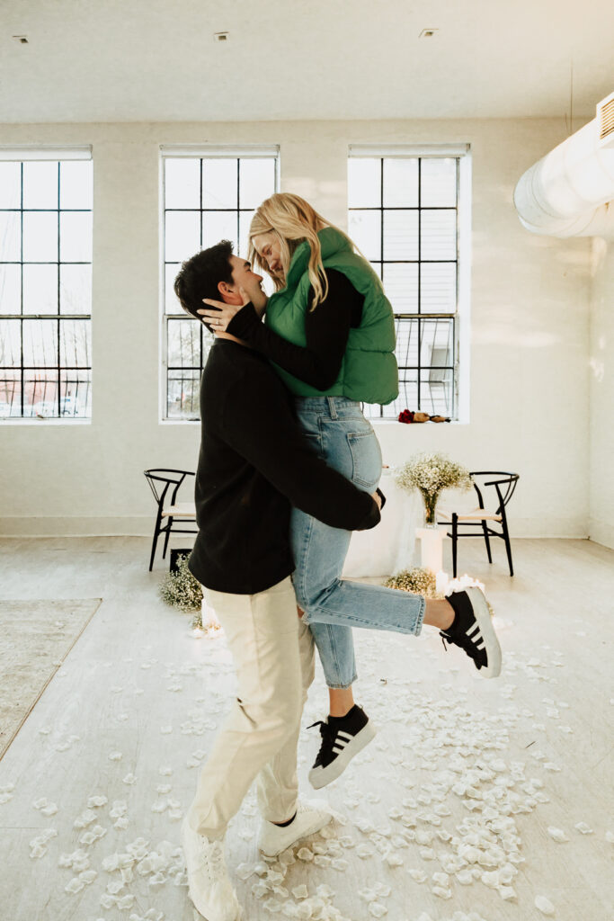 A couple in neutral attire at the Lumen Room Studio in Fort Worth, Texas get engaged surrounded by baby&rsquo;s breath. Photography by Hannah Lylene Photography.