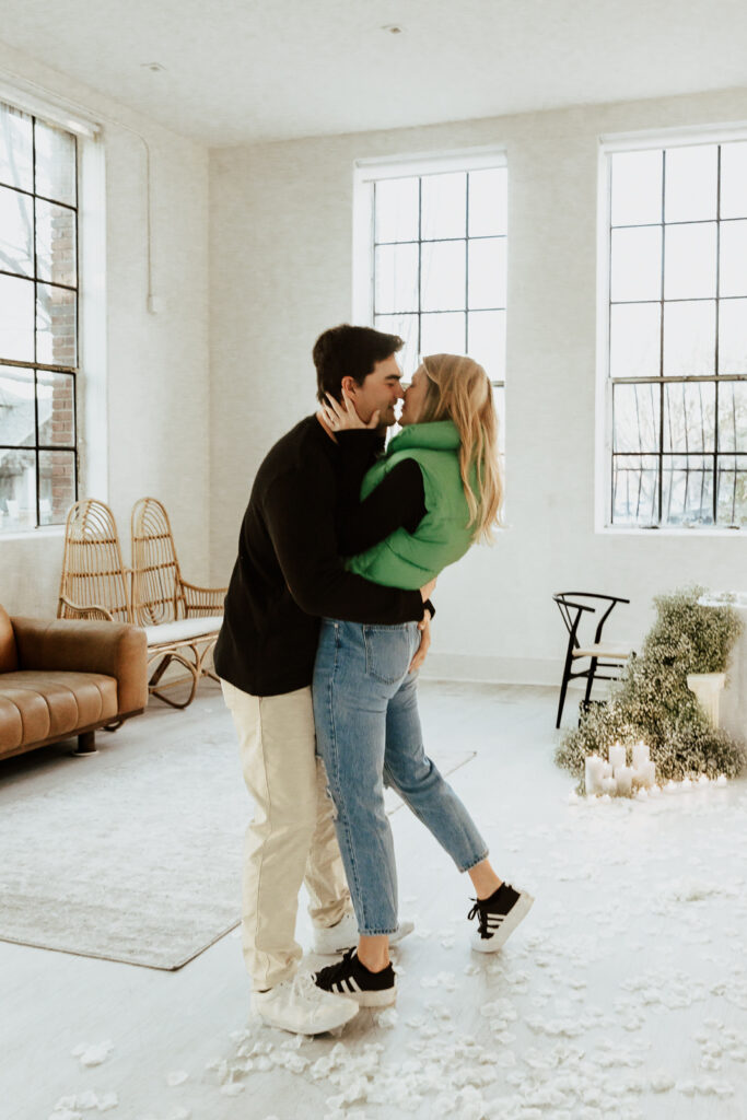 A couple in neutral attire at the Lumen Room Studio in Fort Worth, Texas get engaged surrounded by baby&rsquo;s breath. Photography by Hannah Lylene Photography.