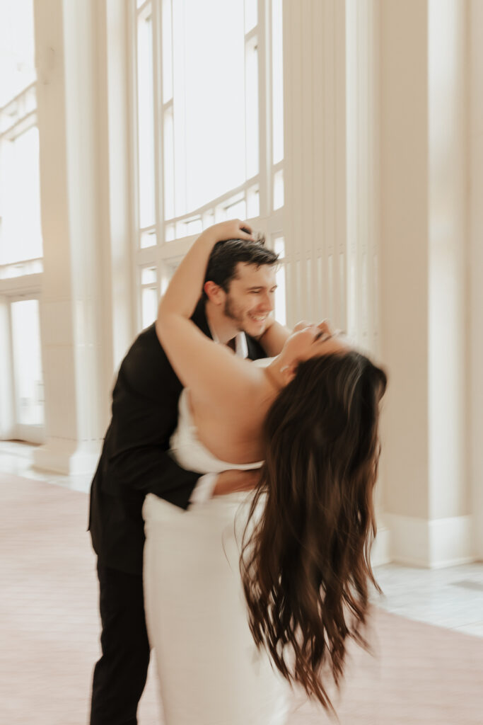 A couple in neutral attire at Bass Hall kiss and run around for engagement photos.