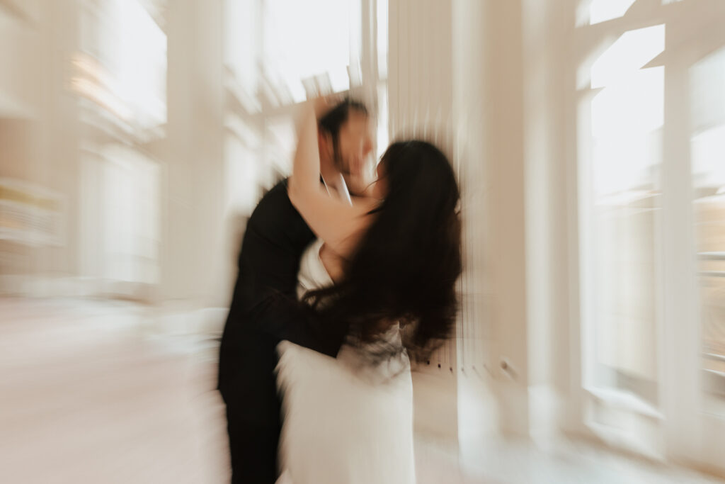 A couple in neutral attire in downtown Dallas Texas kiss and run around for engagement photos.