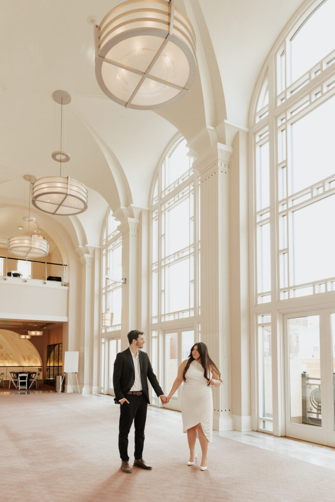 A couple in neutral attire in downtown Dallas Texas kiss and run around for engagement photos.