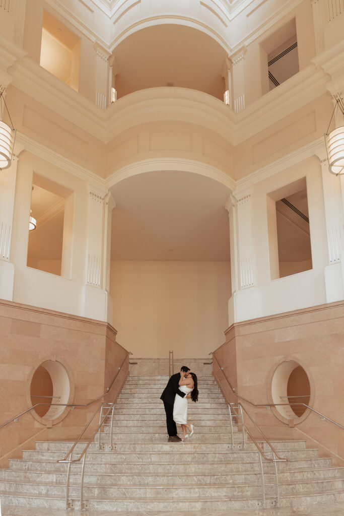 A couple in neutral attire in downtown Dallas Texas kiss and run around for engagement photos. Photography by Hannah Lylene Photography.