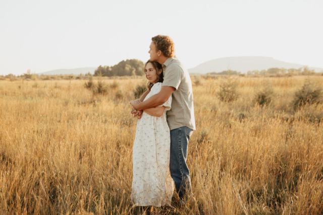 A young couple embrace in an open field
