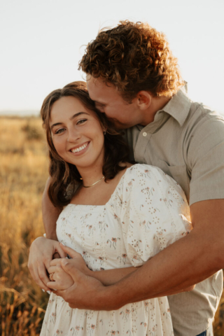 A couple in neutral attire hug in an open field
