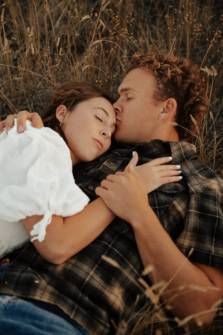 A couple in neutral attire lay down in an open field