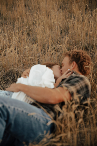 A couple in neutral attire lay down in an open field