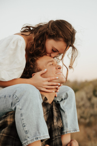 A young woman kisses the forehead while riding a man's shoulder