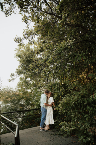 A young couple embrace in the greenery near a field