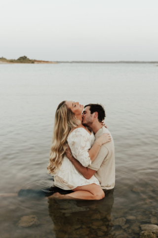 A couple in neutral attire at Grapevine Lake take candid engagement photos.
