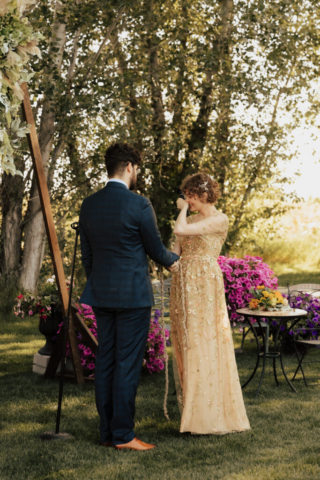 A bride in a golden gown reads her wedding vows to her groom at their outdoor wedding ceremony