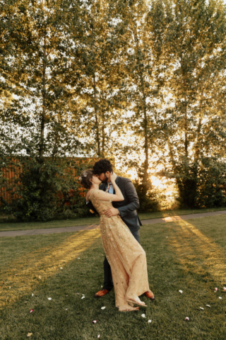 A bride in a gold dress and her groom in a blue suit dance during the golden hour