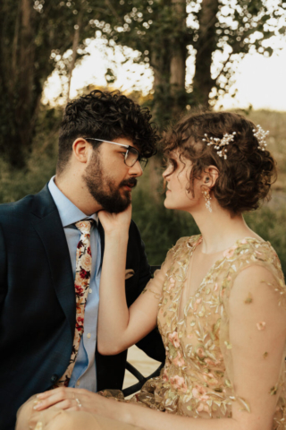 A bride in a gold dress and her groom in a blue suit stare into each other's eyes