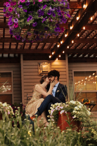 A bride in a gold dress and her groom in a blue suit listen to their wedding speakers