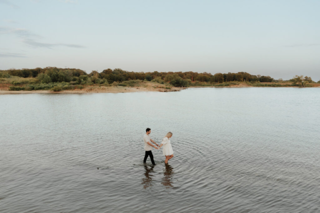 A couple in neutral attire at Grapevine Lake take candid engagement photos.