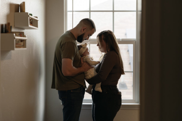 A young couple holds their newborn baby in their nursery to take intimate family photos in Dallas, Texas.