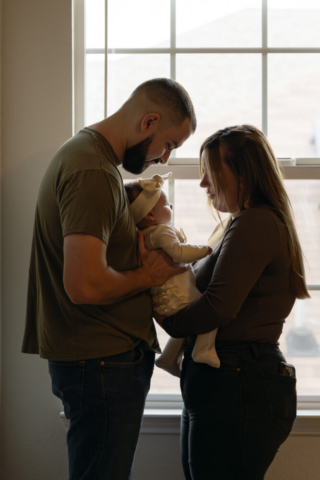 A young couple holds their newborn baby in their nursery to take intimate family photos in Dallas, Texas.