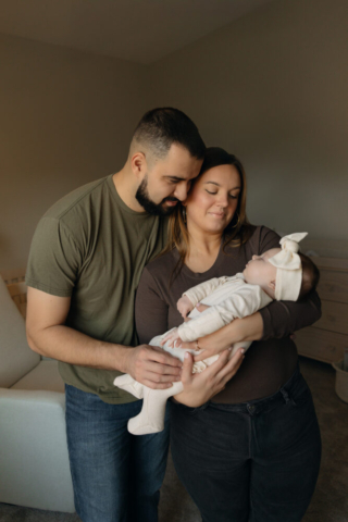 A young couple holds their newborn baby in their nursery to take intimate family photos in Dallas, Texas.