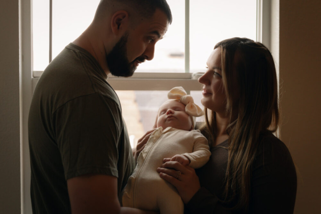 A young couple holds their newborn baby in their nursery to take intimate family photos in Dallas, Texas.