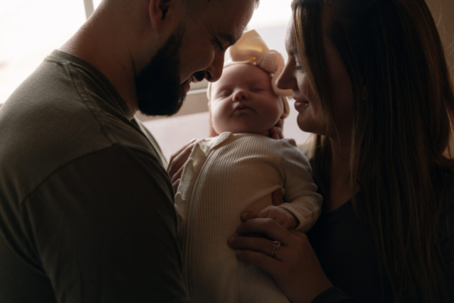 A young couple holds their newborn baby in their nursery to take intimate family photos in Dallas, Texas.