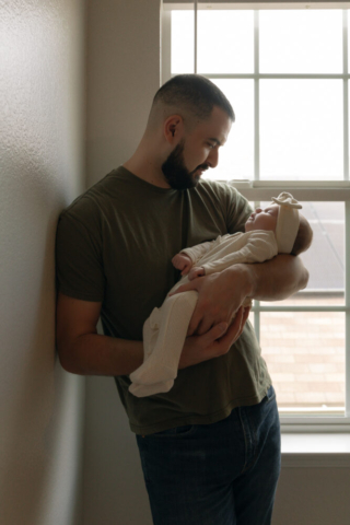 A young couple holds their newborn baby in their nursery to take intimate family photos in Dallas, Texas.