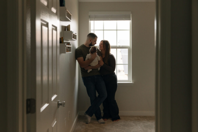 A young couple holds their newborn baby in their nursery to take intimate family photos in Dallas, Texas.