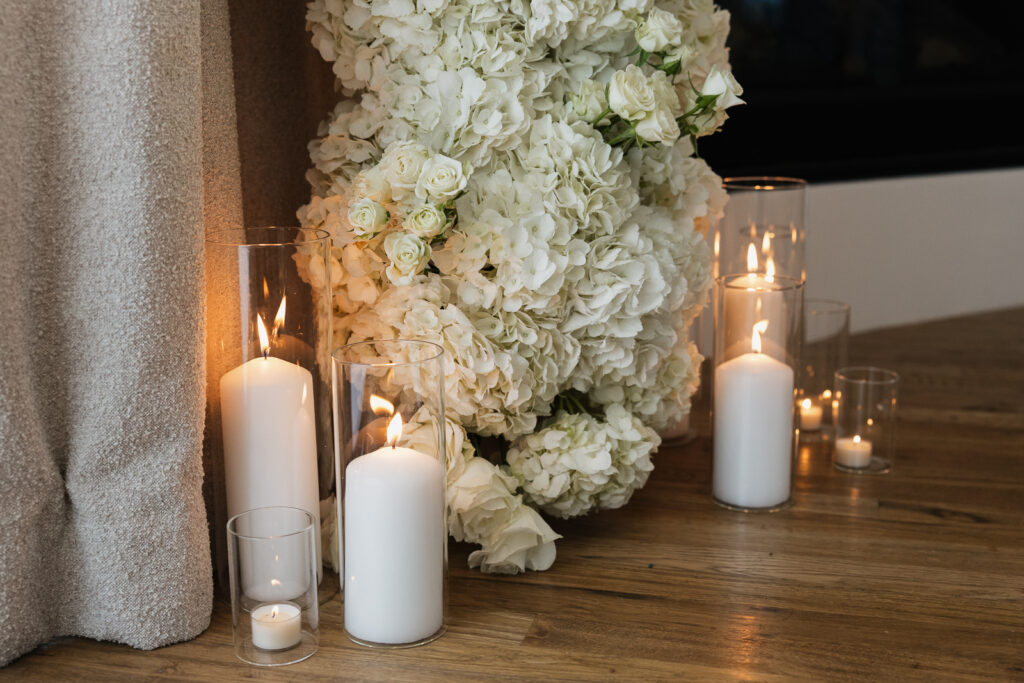 Simple, white candles line the base of a white flower arch in a modern white aesthetic home Timeless indoor wedding in Dallas, captured with a refined, editorial approach.