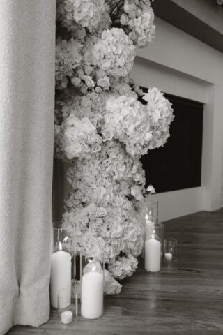Simple, white candles line the base of a white flower arch in a modern white aesthetic home Timeless indoor wedding in Dallas, captured with a refined, editorial approach.